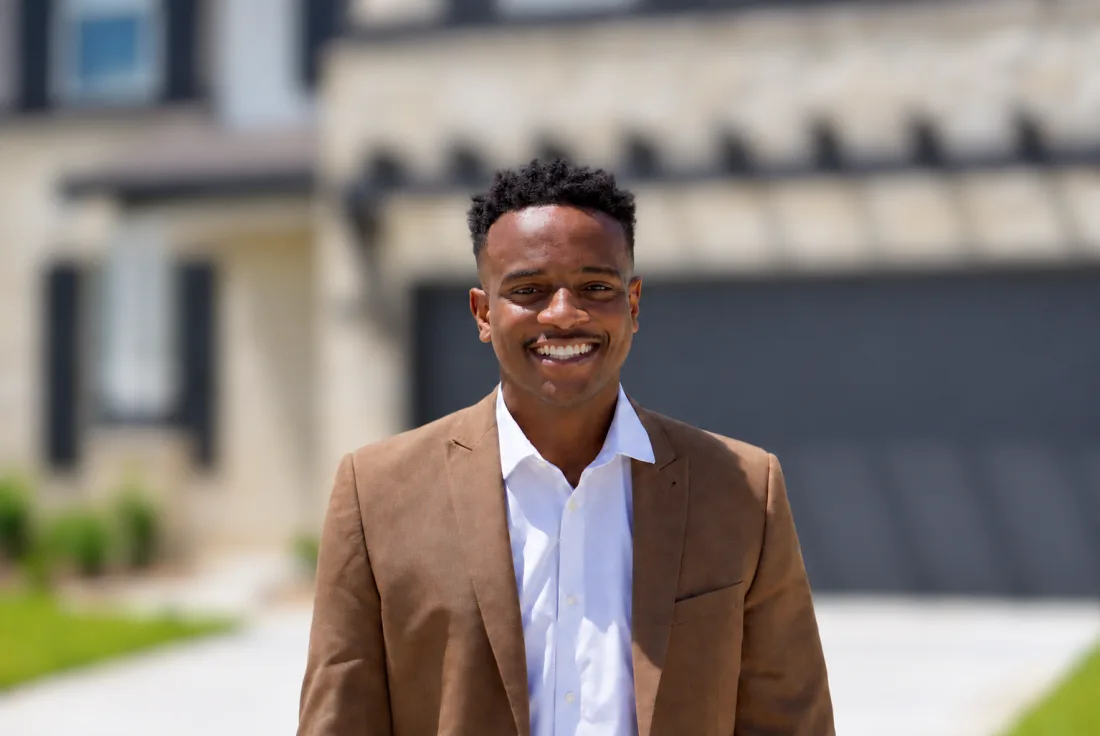 Andrew Bolaji smiling in a brown blazer outdoors